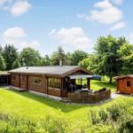 Holzhäuser mit Terrasse und Garten. Auto im Carport. Umgeben von Bäumen.