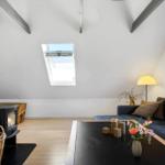 Dachgeschosswohnung mit Holzboden, Schiebedachfenster, Sofa und Kaminofen.