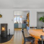 Essbereich mit Holztisch, schwarzen Stühlen und Kamin. Küche mit blauen Schränken sichtbar.