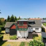Ein zweistöckiges Haus mit Balkon, umgeben von Grün und Bäumen unter blauem Himmel.