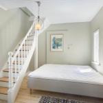 Schlafzimmer mit Bett, Treppe und Fenstern. Wandbild und Deckenleuchte sichtbar.