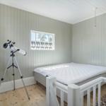 Schlafzimmer mit Bett, Teleskop und Fenster. Holzboden und Paneelen an den Wänden.