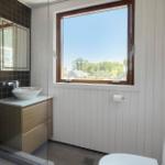 Badezimmer mit Waschbecken, Spiegel und großem Fenster mit Blick auf Außenbereich.