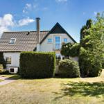 Haus mit Garten, Balkon und Schornstein unter blauem Himmel.