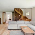 Wohnzimmer mit hellem Sofa, Holzfußboden und Wendeltreppe mit integrierten Regalen.