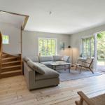 Wohnzimmer mit Sofa, Tisch und Sessel. Holzdielenboden und Fenster zur Außenterrasse.