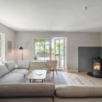 Wohnzimmer mit Sofa, Kamin und Fenstern zum Garten.