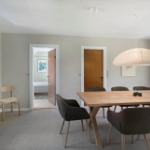 Esszimmer mit Holztisch, Stühlen und Deckenleuchte. Durchgang zu Schlafzimmer und Tür.