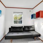 Schwarzes Sofa mit Kissen, Fenster und Wandregale in einem Raum mit weißen Wänden.