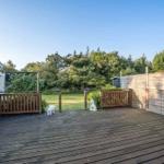 Terrasse mit Tisch, Zaun und Garten. Hintergrund: Bäume und klarer Himmel.