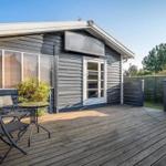 Terrasse mit Tisch und Stühlen vor einem Holzhaus mit Fenstern und Tür.