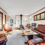 Wohnzimmer mit braunen Ledermöbeln, Kamin und großen Fenstern.