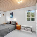Schlafzimmer mit Holzdecke, Bett, Fenstern und Schrank. Weiße Wände und Holzmöbel.