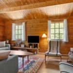 Wohnzimmer mit Holzwand, Sofa, Sessel, Fernseher und Kaminofen.