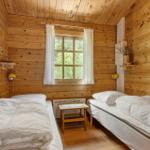Zwei Einzelbetten mit weißen Bettwäschen, Holzwand und Fenster mit weißen Vorhängen.