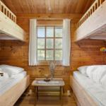 Zimmer mit zwei Etagenbetten, Holzwand und Fenster mit weißen Vorhängen.
