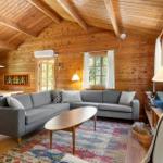 Wohnzimmer mit Holzwand, grauem Sofa und Holztisch auf gemustertem Teppich.