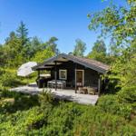 Holzhütte mit Terrasse, Gartenmöbeln und Sonnenschirm in grüner Umgebung.