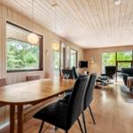 Essbereich mit Holztisch und schwarzen Stühlen. Im Hintergrund Wohnbereich mit Sitzmöbeln und Kamin.