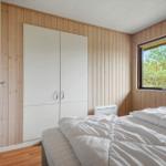 Schlafzimmer mit Bett, Kleiderschrank und Fenster mit Blick auf Wald.