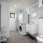 Badezimmer mit Waschmaschine, Spiegel, Toilette und Fenster.