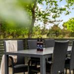 Terrasse mit Tisch und Stühlen, zwei Bierflaschen und Blick auf Bäume.