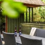 Terrasse mit Tisch, Stühlen und zwei Bierflaschen vor einem Holzhaus mit Dach.