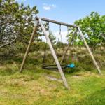 Holzschaukel mit blauem Sitz im Gras unter Bäumen