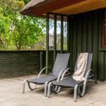 Zwei Liegestühle auf einer Terrasse vor einem Haus mit Holzwand und Dach.