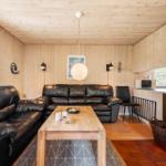 Wohnraum mit Ledersofa, Holztisch und Kaminofen. Holzwände und -decke. Küche mit Mikrowelle.