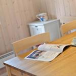 Holztisch mit Stuhl, Tasse und Zeitschrift. Holzwände und Fenster im Hintergrund.