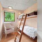 Zimmer mit Doppelstockbett, Stuhl und Fenster mit Blick auf Wald.