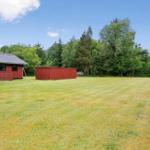 Roter Holzhaus mit Garten und Wald im Hintergrund.