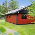 Rotes Holzhaus mit schwarzem Dach in grüner Umgebung.