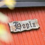 Holzschild mit Schriftzug Hopla an roter Holzwand.