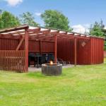 Roter Holzüberdachter Bereich mit Tisch, Stühlen und Feuerkorb auf grünem Rasen.