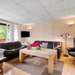 Wohnzimmer mit Sofa, Sessel, Tisch und Fernseher. Holzwände und große Fenster.