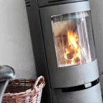 Moderne Holzofen mit brennendem Feuer, daneben Sessel und Korb.