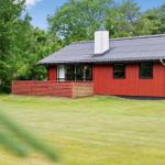 Rotes Holzhaus mit grauem Dach und Garten. Umgeben von Bäumen und Gras.