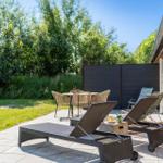 Terrasse mit Liegen, Tisch und Stühlen neben einem roten Backsteinhaus.
