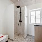 Badezimmer mit Dusche, Waschbecken und Toilette. Weiße Fliesen und Holzoptik.