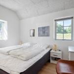 Schlafzimmer mit Bett, zwei Fenstern und einem braunen Stuhl.