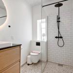 Badezimmer mit Dusche, Waschbecken und Toilette. Weiße Fliesen und Holzschränke.