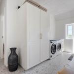 Wäscherei mit Waschmaschine, Trockner und Schrank. Fenster und Tür führen nach draußen.