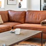 Ein braunes Ledersofa mit Kissen und Decke steht vor einem Holztisch mit Tassen.