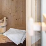 Sauna mit Holzbank, Holzkanister und weißem Handtuch.
