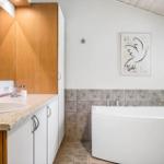 Badezimmer mit Badewanne, Waschbecken und Holzschränken. Wandbild mit Friedensmotiv.