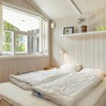 Schlafzimmer mit Holzwand, Fenster und Bett mit weißen Bettwäsche.