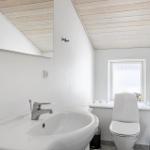 Badezimmer mit Waschbecken, Toilette und Fenster. Holzdecke und Spiegel sichtbar.