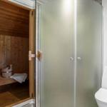 Dusche mit Duschwand, Toilette und integrierte Sauna mit Holzbank und Eimer.